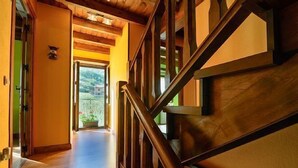 Un escalier en bois mène à un balcon d’où l’on peut admirer un paysage verdoyant et un bâtiment situé au loin.