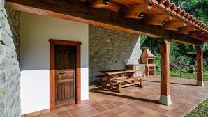 Une terrasse couverte avec un mur en pierre, une porte en bois et une table de pique-nique.