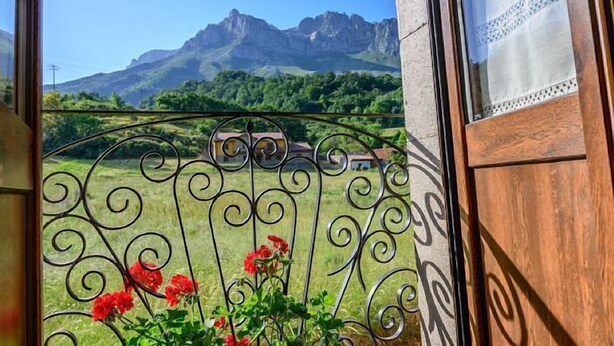 Un balcon agrémenté d’une grille en fer forgé, une vue sur des champs verdoyants et des montagnes lointaines.