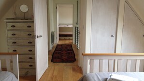 Une chambre à coucher avec une commode en bois, un lit doté d’une tête de lit blanche et un petit miroir rond posé sur la commode.