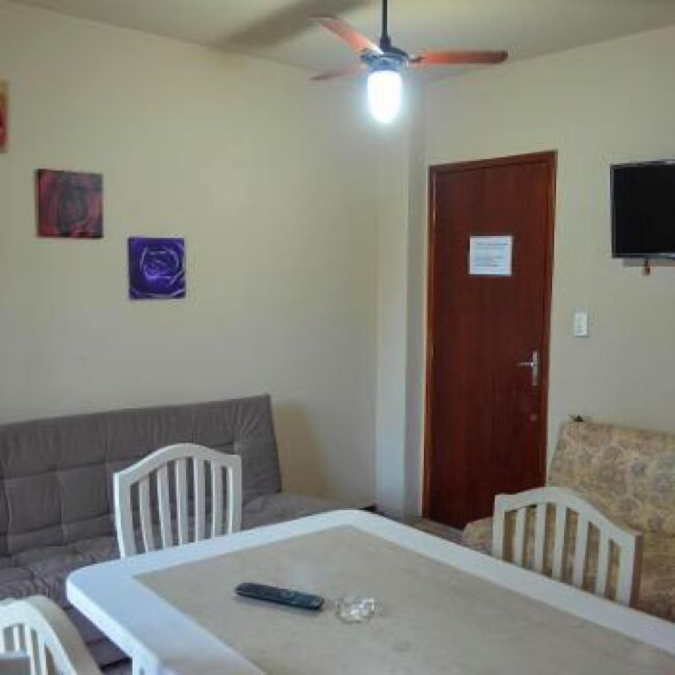 A room with a dining table, chairs, a ceiling fan, a television, and artwork on the walls.