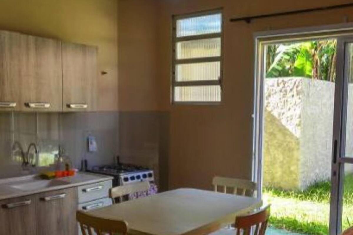 A compact kitchen with wooden cabinets, a gas stove, and a dining area with two chairs.