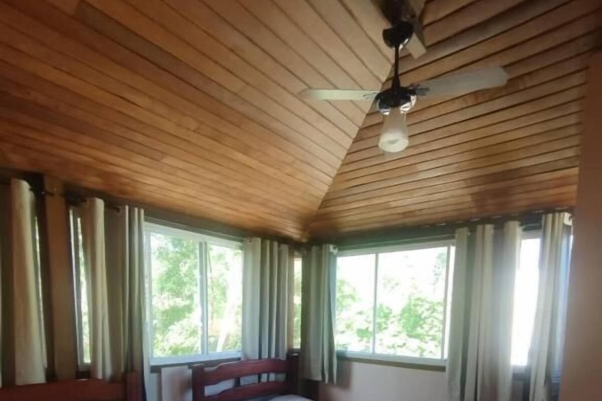 A room with two beds, wooden ceiling, and large windows with curtains.