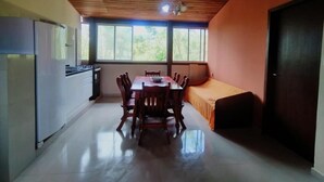A kitchen with a dining table and chairs, a sofa, and a window with a view of greenery. - Apart da Cachoeira (Florianópolis)