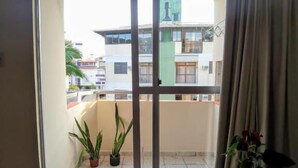 A balcony with a sliding glass door, potted plants, and a view of neighboring buildings. - Apart da Cachoeira (Florianópolis)