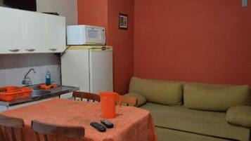 Un espacio habitable compacto con kitchenette, una mesa de comedor con mantel rojo, un sofá y un televisor montado en la pared.