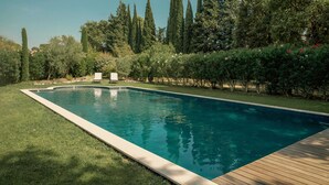 A rectangular swimming pool with a wooden deck edge, surrounded by well-maintained grass and various trees. - Opulent Villa with newly renovated heated pool. 5 minute drive to center (Saint-Rémy-de-Provence)