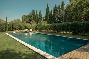 A rectangular swimming pool with a wooden deck edge, surrounded by well-maintained grass and various trees. - Opulent Villa with newly renovated heated pool. 5 minute drive to center (Saint-Rémy-de-Provence)