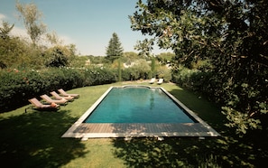 Une piscine rectangulaire dotée d’une terrasse en bois, entourée d’une pelouse bien entretenue et de divers arbres.