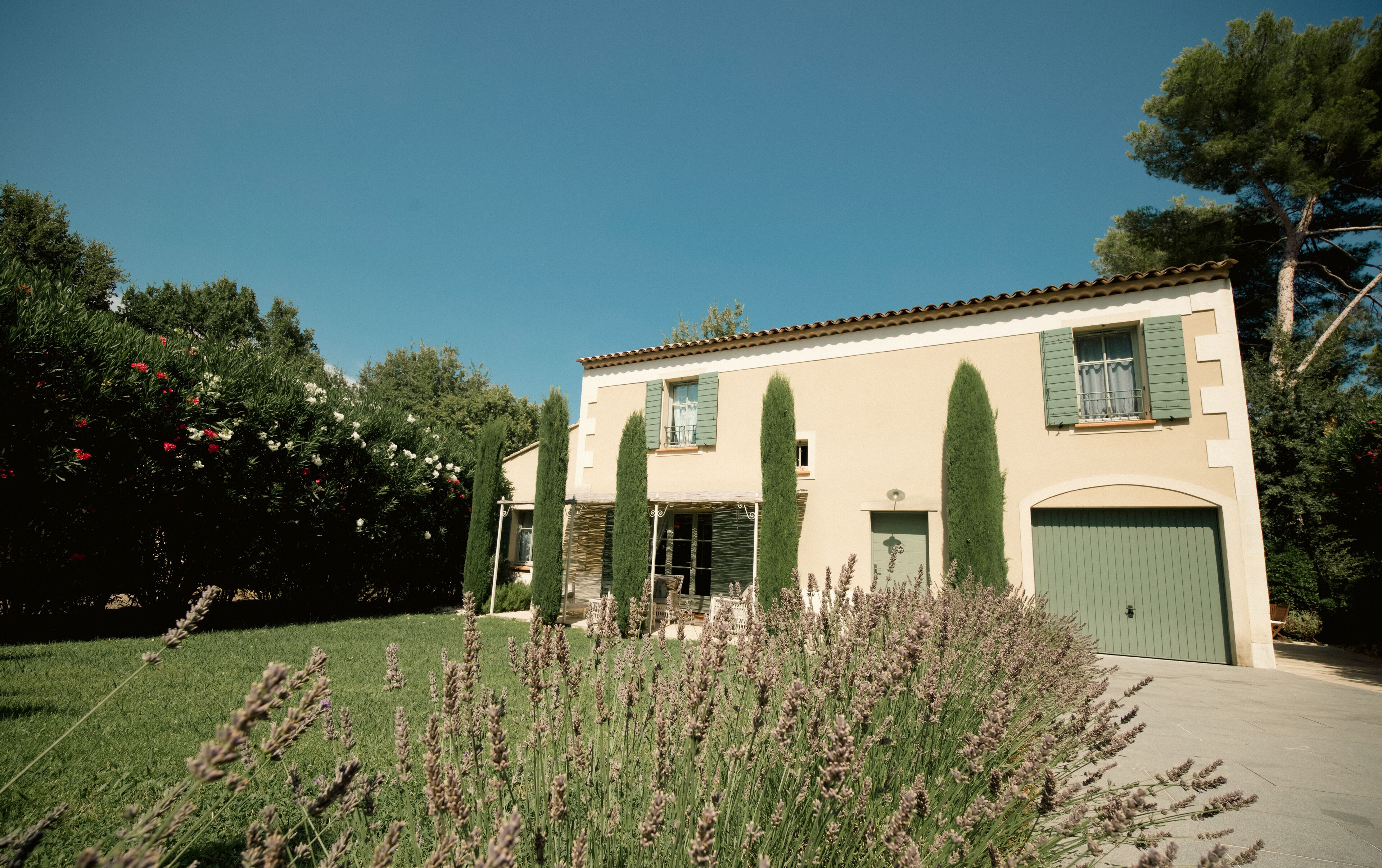 Un edificio de dos pisos con una puerta verde, un balcón y un jardín con plantas de lavanda.