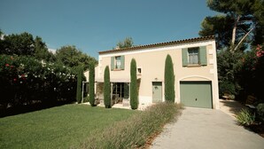 A two-story house with a green door, a covered porch with chairs, and a well-maintained lawn. - Opulent Villa with newly renovated heated pool. 5 minute drive to center (Saint-Rémy-de-Provence)