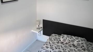 Un dormitorio con cama, una mesita de noche con lámpara, y dos cuadros en la pared.