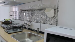 A kitchen with a stainless steel sink, a microwave, and a rack holding various kitchen utensils.