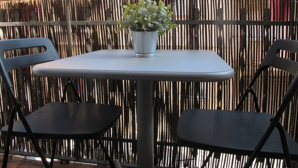A balcony with a table and two chairs, a potted plant, and a bamboo fence.