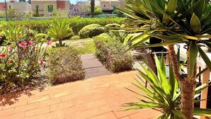 Un sendero empedrado que conduce a un edificio de techo en tejas, rodeado de diversas plantas y flores.