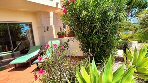 Un edificio moderno con un balcón, plantas en macetas y una zona de césped verde.