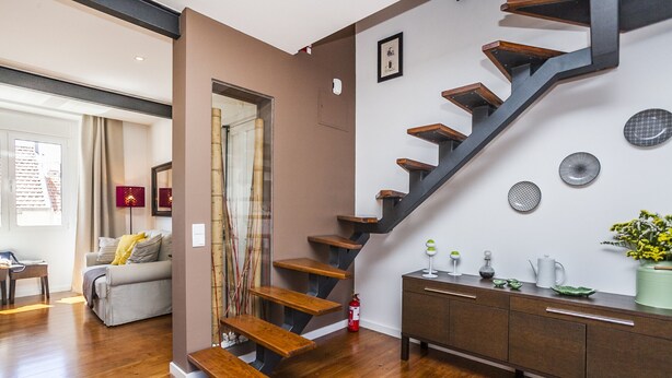 Un interior modern amb una escala, terres de fusta, un sofà i un armari.