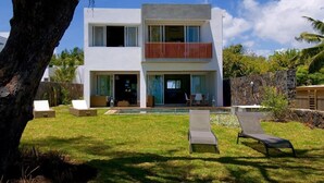 Una casa moderna de dos pisos con balcón, piscina y mobiliario de exterior.