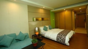 A modern hotel room with a bed, a sofa, a nightstand with a lamp, and a potted plant. - F&H Apartment Guangzhou Wales Branch (Guangzhou)