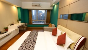 A modern hotel room with a large bed, a desk, a chair, a window with a city view, and a mounted mirror. - F&H Apartment Guangzhou Wales Branch (Guangzhou)