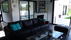 A modern living room with a black leather sofa, a glass coffee table, and a large window offering a view of the outdoors.
