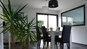 A modern dining area with a white table and black chairs, a potted plant, and a large window with a view of greenery.
