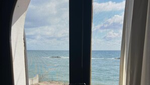 A window with a view of the ocean, a grassy area, and a patio with a table and chairs. - Villa Mary in Pula: exclusive location with private access to the beach (Pula)