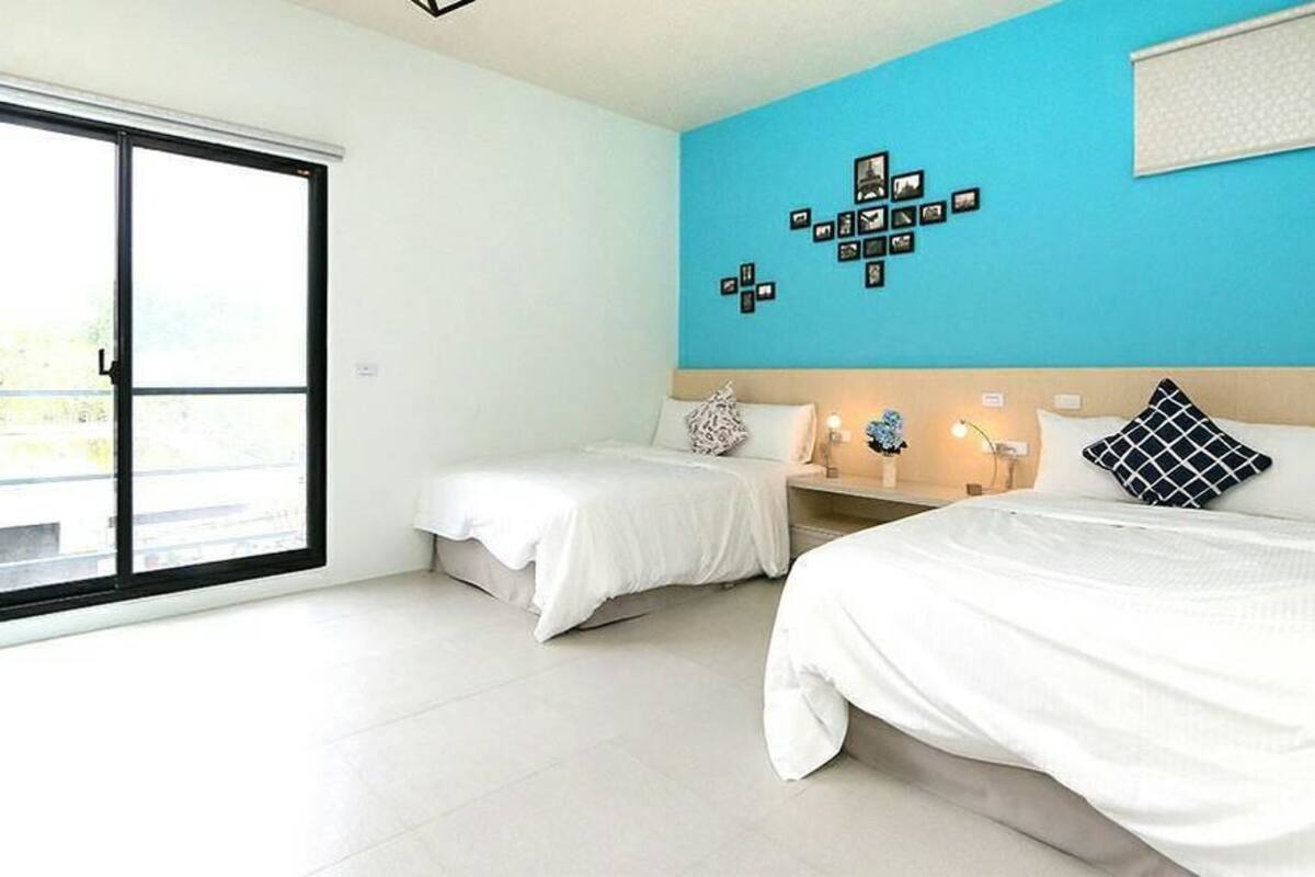 A hotel room with two beds, a large window, and a blue accent wall.