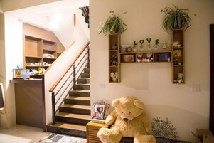 A cozy living area with a large teddy bear, a staircase, and shelves with decorative items.
