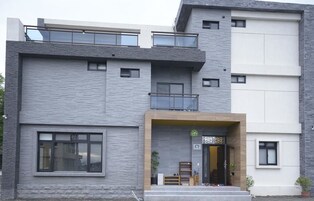 A modern multi-story building with a grey stone facade, large windows, and a balcony.