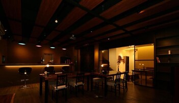 Un restaurante tenuemente iluminado con vigas de madera en el techo, una zona de bar y varias mesas y sillas.