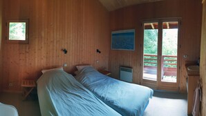 A wooden cabin room with two beds, a small window, and a door leading to an outdoor balcony.