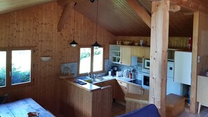 A wooden cabin interior with a kitchen area, wooden walls, and a dining space.