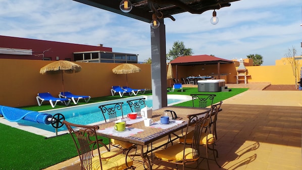 A poolside area with a table and chairs, a hot tub, and lounge chairs. - beautiful villa with heated pool, outdoor hot tub, free wifi (Antigua)