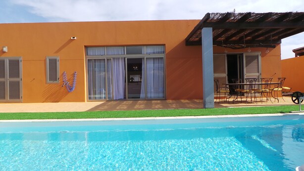 A modern building with a swimming pool, large glass doors, and outdoor furniture.