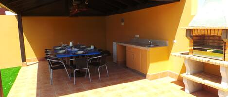 Un patio exterior con una mesa de comedor para cuatro personas, una parrilla y una pequeña área de cocina.