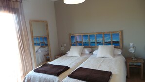 A double bed with two pillows, a wooden headboard, and a painting of a coastal scene.