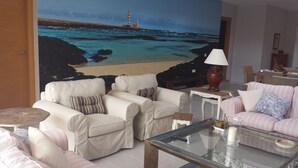A living room with two sofas, a glass coffee table, and a painting of a coastal scene.