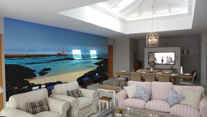 A living room with a beach mural, a dining area, and a sofa with striped cushions.