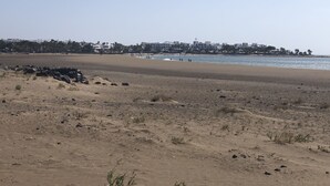 Een strand met een zandstrand, enkele verspreide rotsen en een horizon vol gebouwen langs de kust.