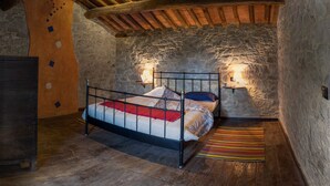 Un dormitorio rústico con paredes de piedra, estructura de cama de metal, suelo de madera y un armario de madera.