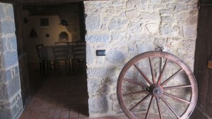 Una habitación con paredes de piedra, una puerta de madera rústica, una rueda grande y suelo de ladrillo.
