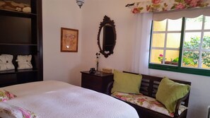 Quarto com cama grande, penteadeira, espelho e janela com vista para o verde.