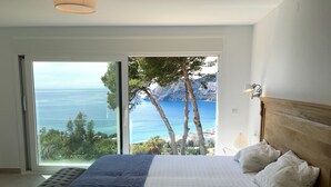 Een slaapkamer met een groot bed, uitzicht op zee en een balkon.