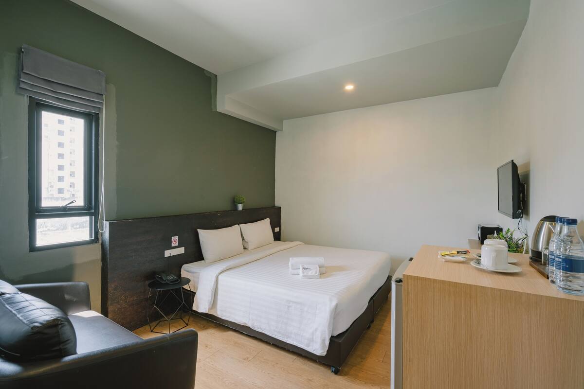 A hotel room with a bed, bedside table, and a small desk with a chair.