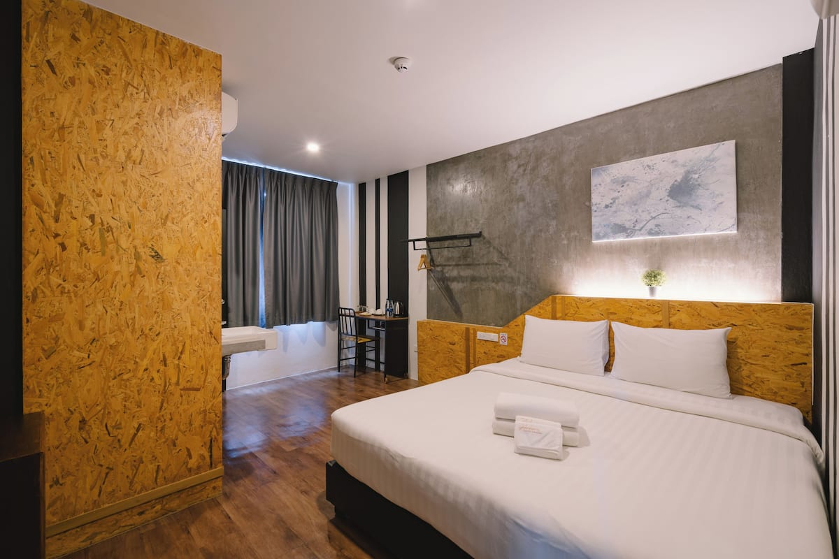 A hotel room with a wooden headboard, a bed with white linens, a desk with a chair, and a large window with curtains.