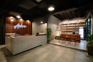 A modern reception area with a wooden reception desk, a neon sign, and a bar area with shelves of bottles and a refrigerator. - The Arbern Hostel x Bistro (Phuket)