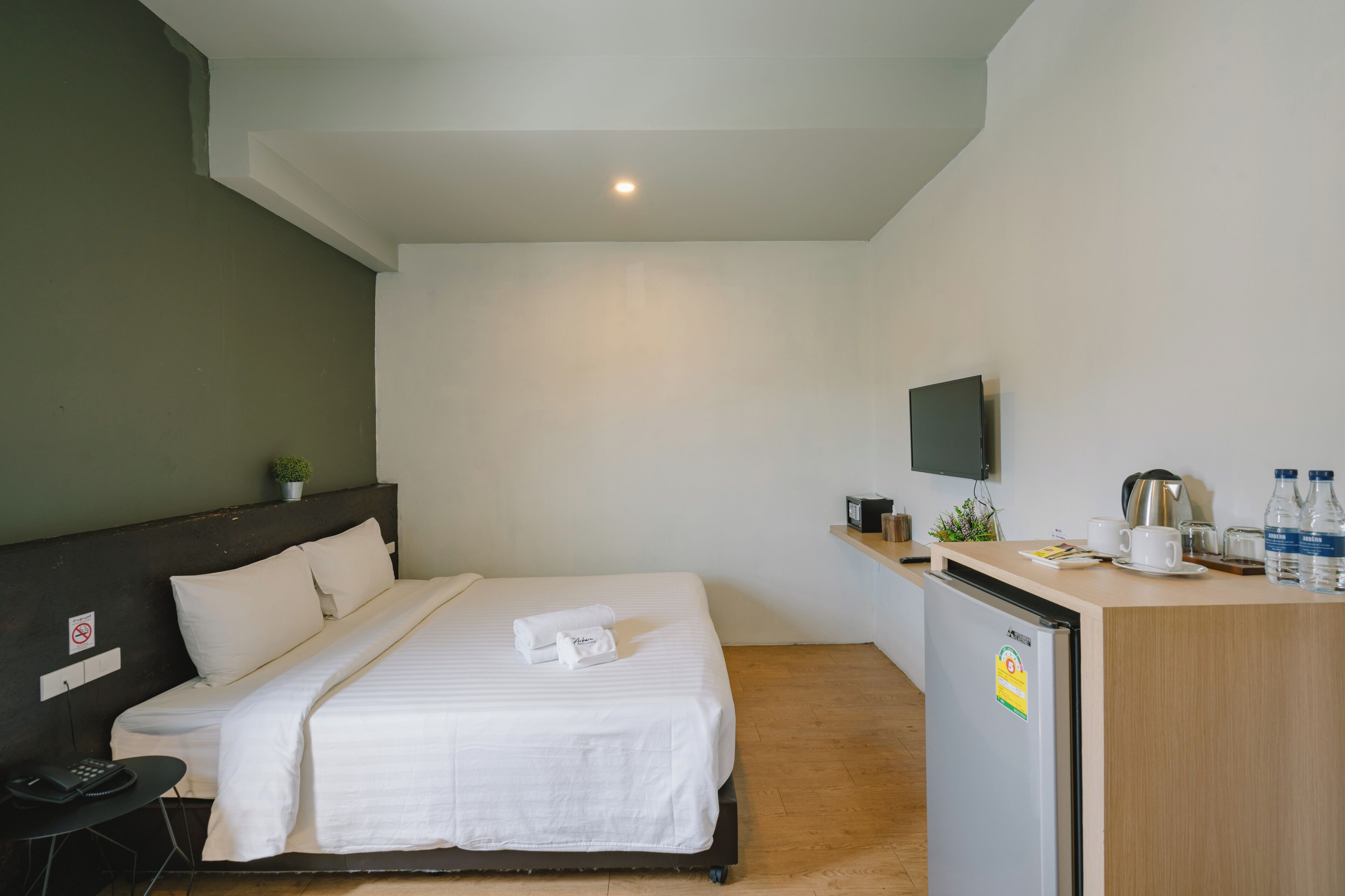 A hotel room with a bed, a desk with a refrigerator, a television, and a small plant.