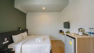 Habitación de hotel con cama, escritorio con refrigerador, televisión y una planta pequeña.