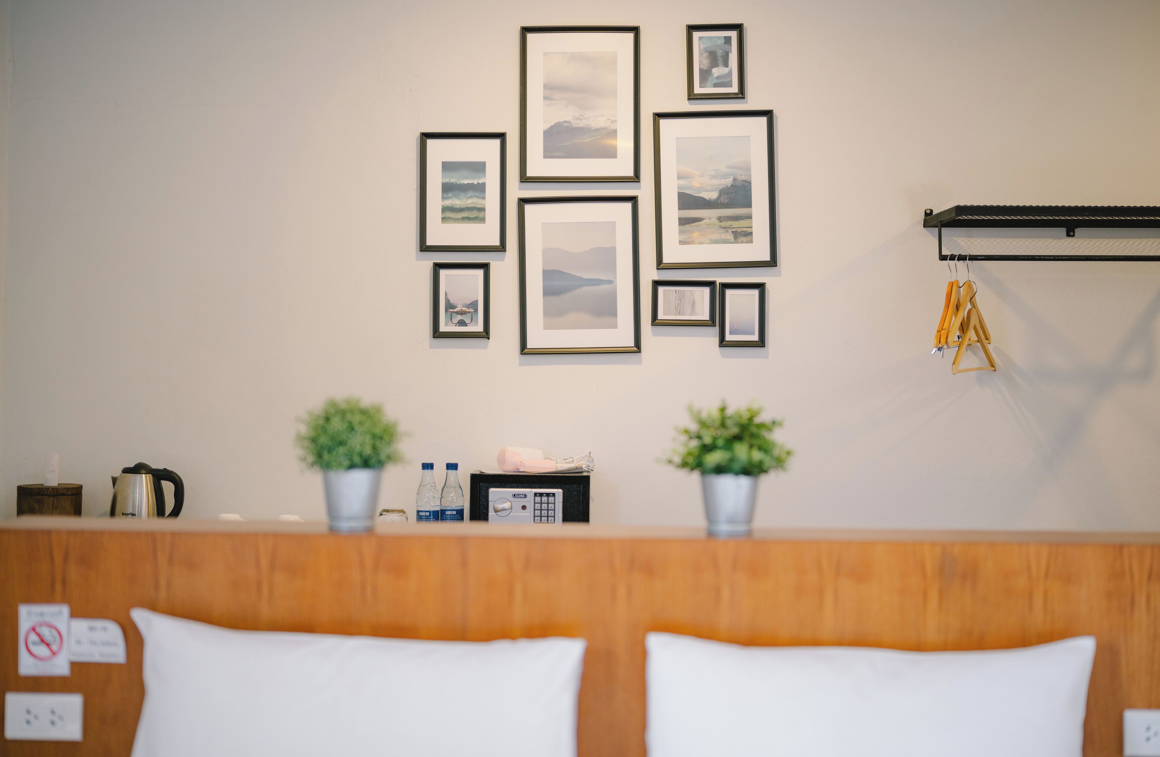 A hotel reception area with framed artwork on the wall, a wooden reception desk, two potted plants, and a coat rack with hangers.